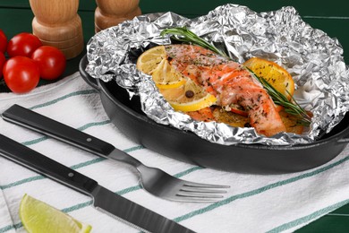Photo of Tasty salmon baked in foil with citrus fruits and rosemary served on green table, closeup