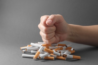 Photo of Stop smoking. Woman crushing cigarettes on grey background, closeup