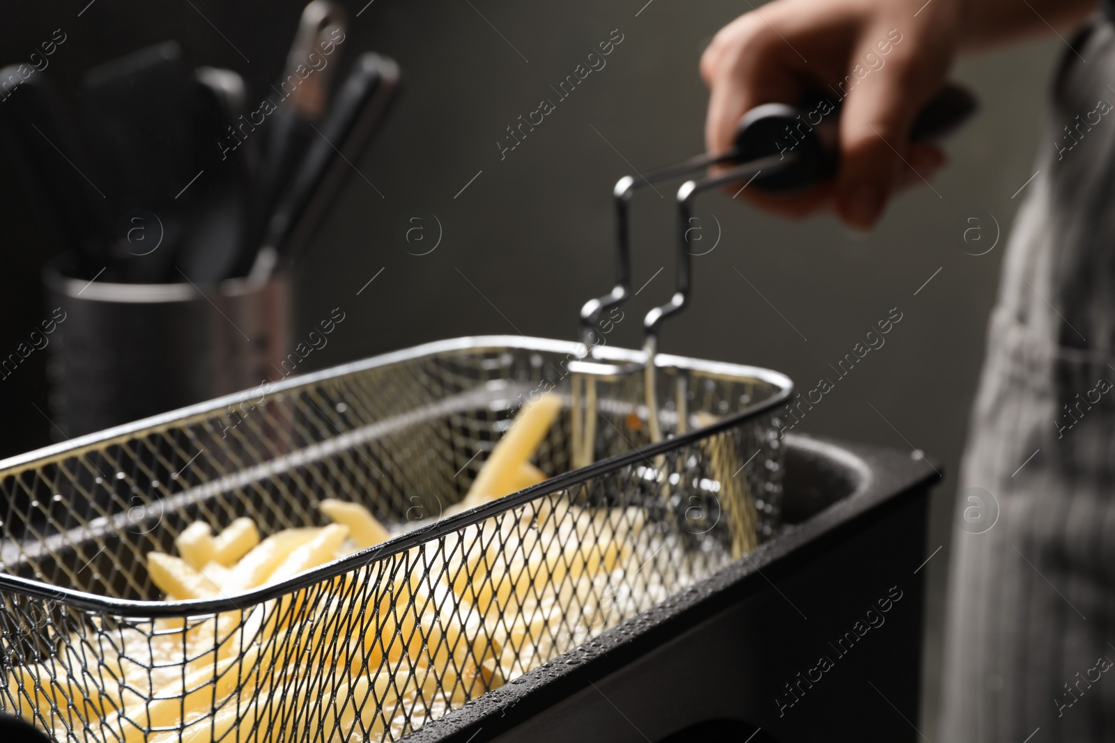 Photo of Chef cooking delicious french fries in hot oil, closeup