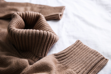 Photo of Brown warm sweater on white crumpled fabric, closeup