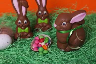 Photo of Easter celebration. Funny chocolate bunnies with candies and painted egg on grass against red background