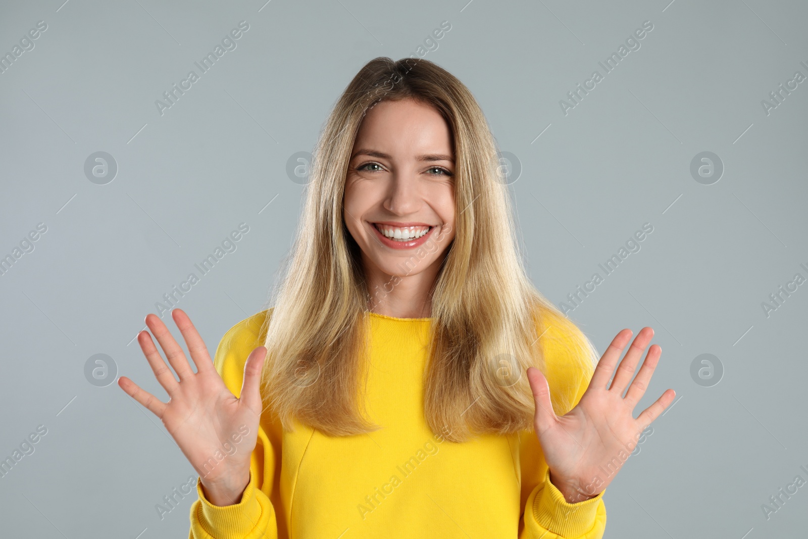 Photo of Woman showing number ten with her hands on light grey background