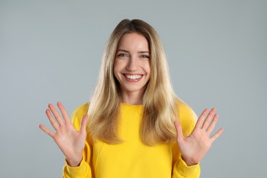 Woman showing number ten with her hands on light grey background