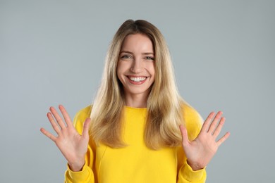 Photo of Woman showing number ten with her hands on light grey background