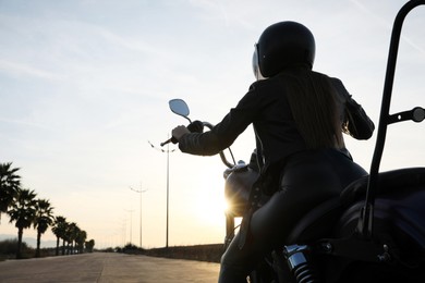 Photo of Woman with helmet riding motorcycle at sunset, back view. Space for text