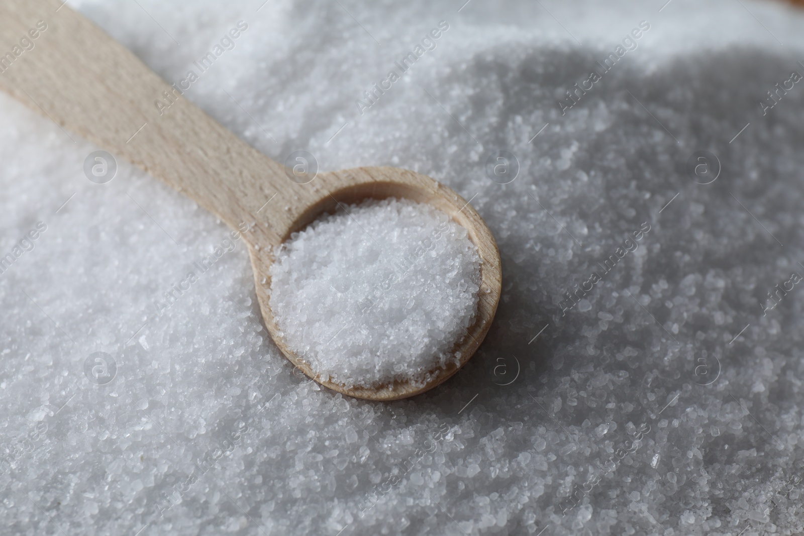 Photo of Wooden spoon on white sea salt, closeup