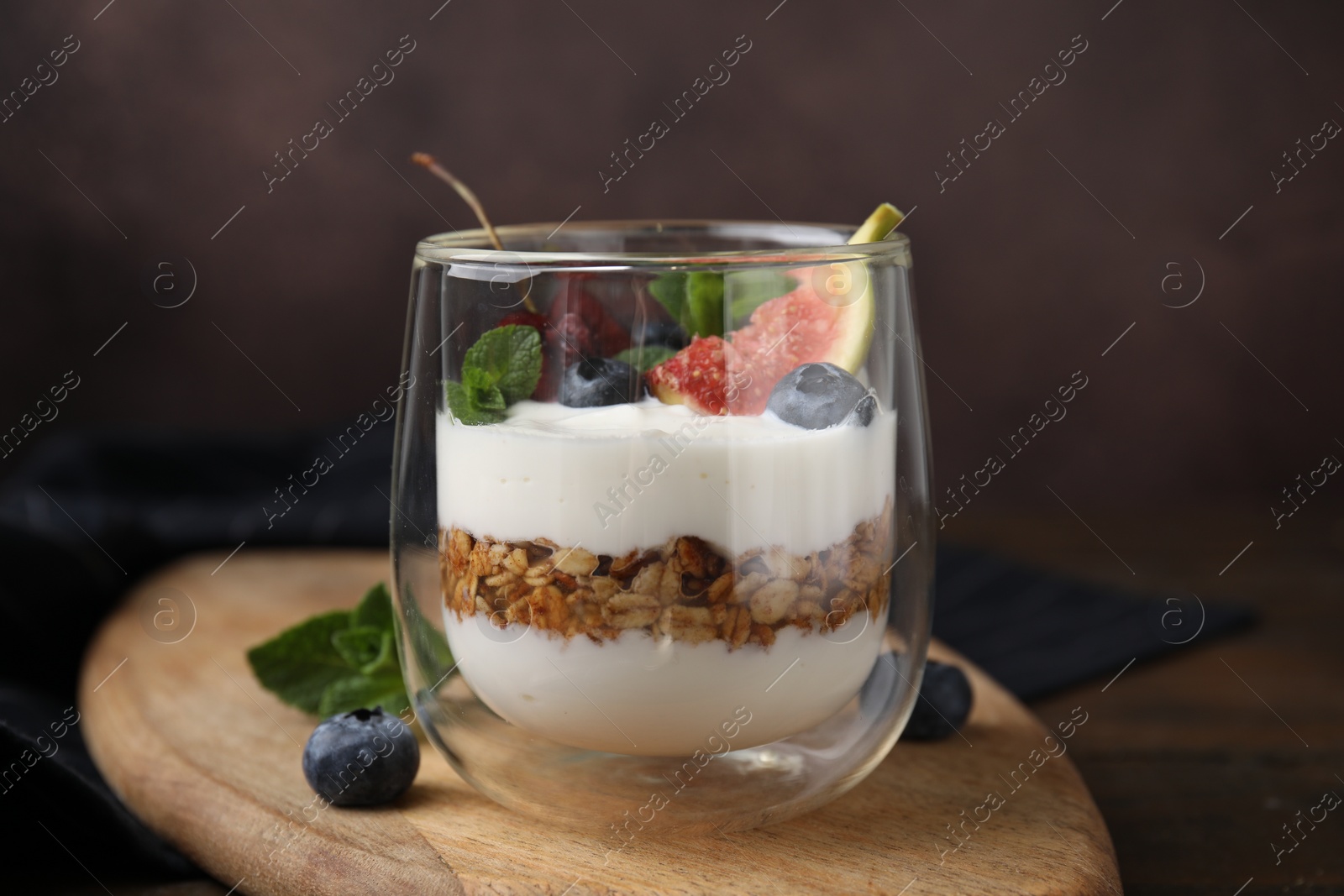 Photo of Glass with yogurt, berries, mint and granola on wooden table, closeup