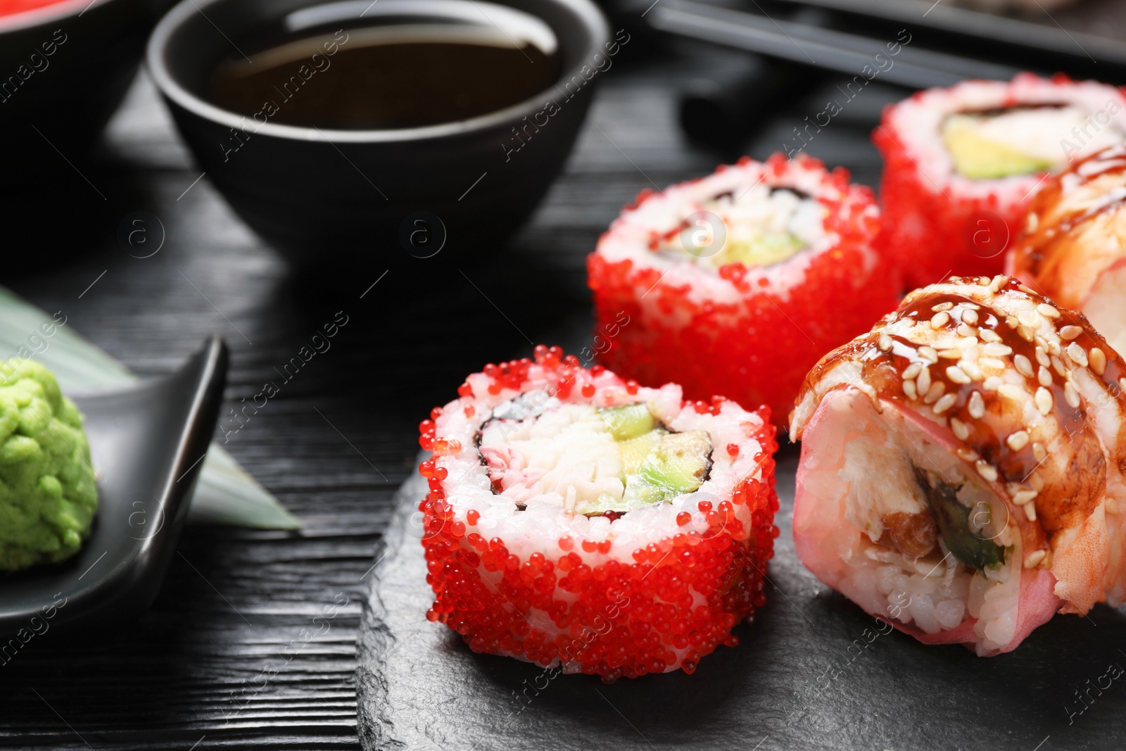 Photo of Different sushi rolls on black wooden table, closeup