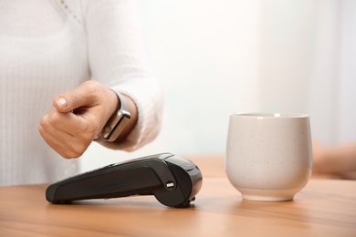 Woman using terminal for contactless payment with smart watch in cafe