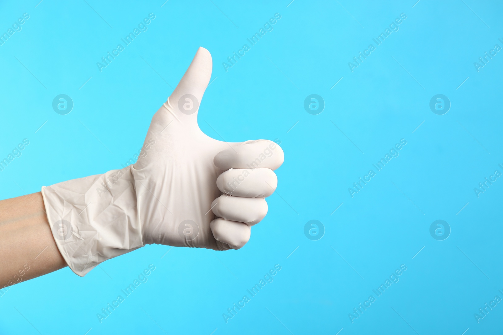 Photo of Person in medical gloves showing thumb up on light blue background, closeup of hand. Space for text