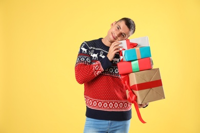 Happy man in Christmas sweater holding gift boxes on yellow background