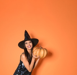 Photo of Beautiful woman wearing witch costume with pumpkin for Halloween party on yellow background, space for text