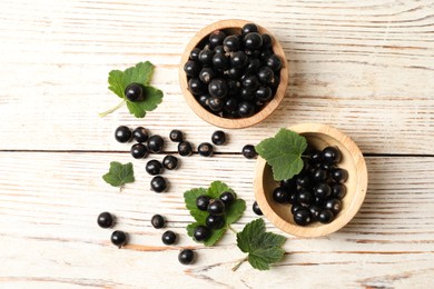 Photo of Ripe blackcurrants and leaves on light wooden table, flat lay