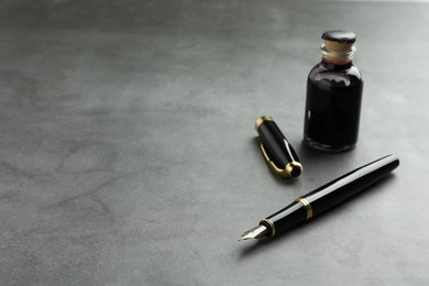 Photo of Stylish fountain pen, bottle of ink and inkwell on grey textured table, space for text