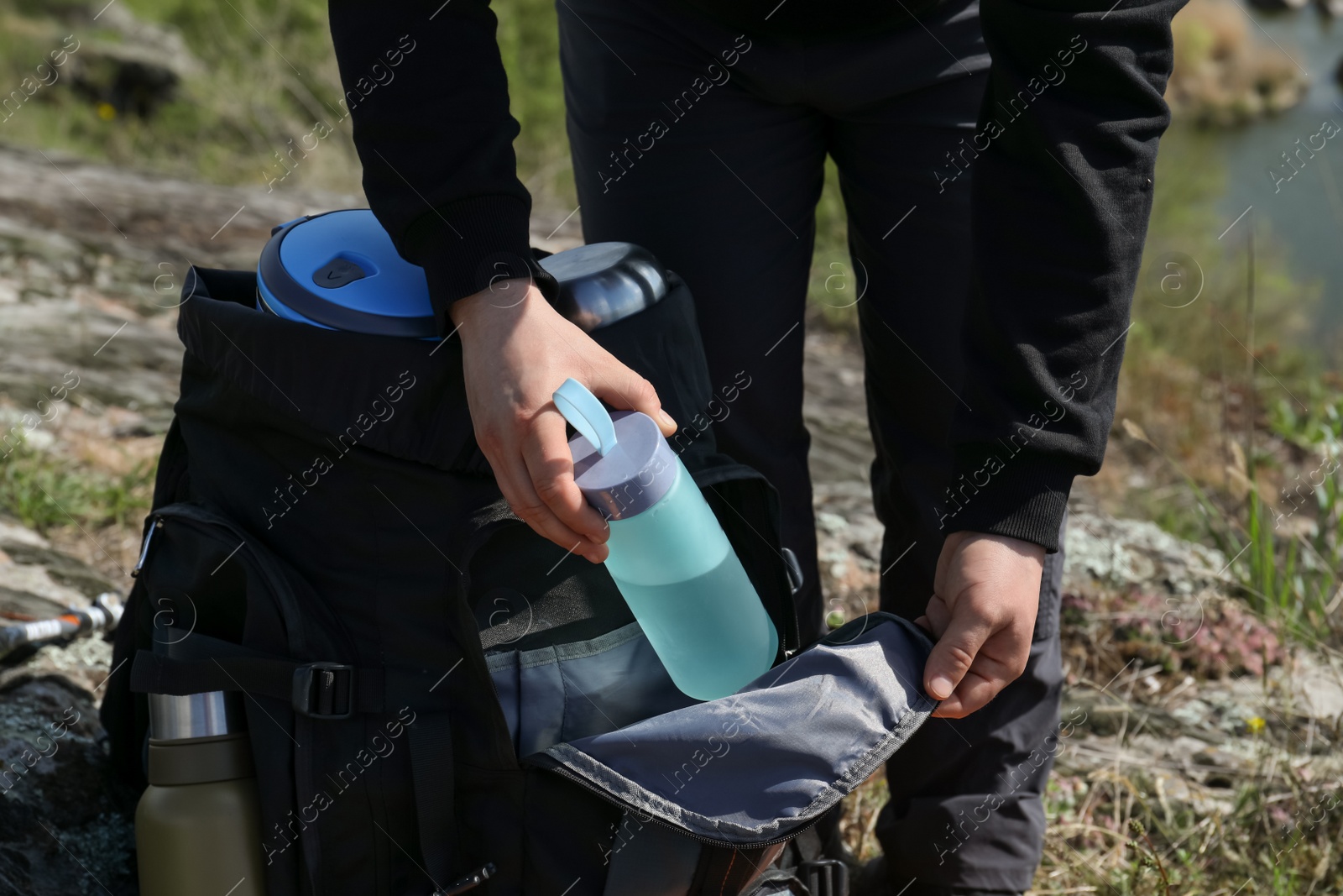 Photo of Hiker putting bottle of water into backpack outdoors, closeup