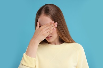 Photo of Embarrassed woman covering face with hand on light blue background