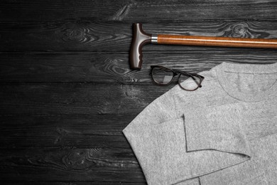 Elegant walking cane, sweater and glasses on black wooden table, flat lay. Space for text