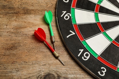 Dart board with color arrows on wooden background