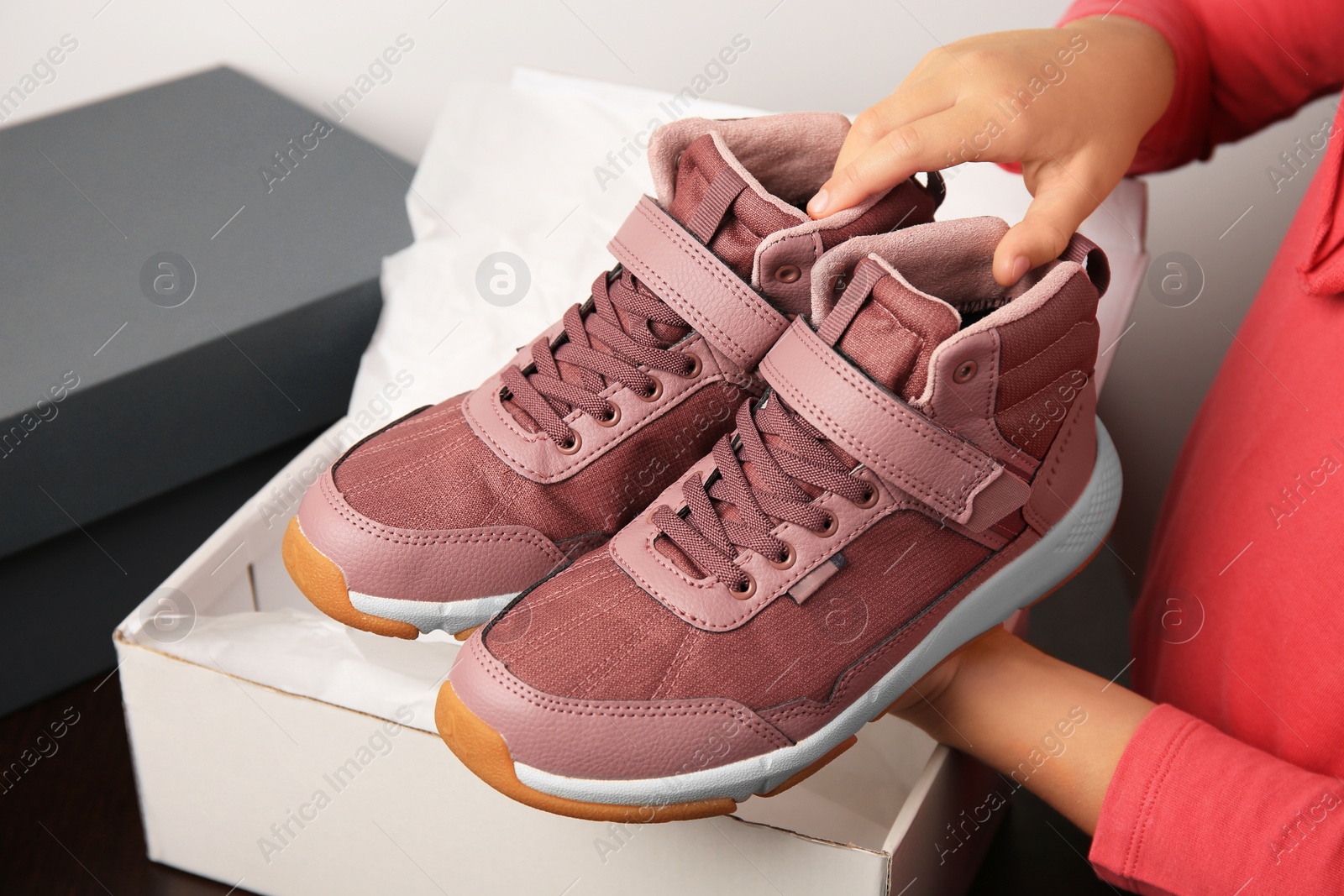 Photo of Girl taking out new sneakers from box against light grey background, closeup