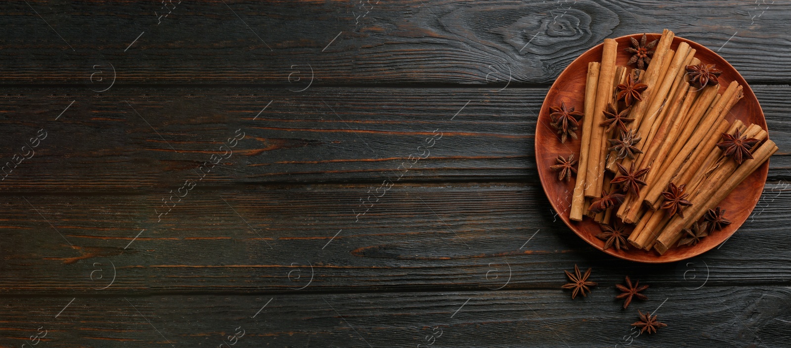 Image of Aromatic cinnamon sticks and anise on black wooden table, flat lay with space for text. Banner design