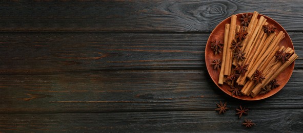 Aromatic cinnamon sticks and anise on black wooden table, flat lay with space for text. Banner design