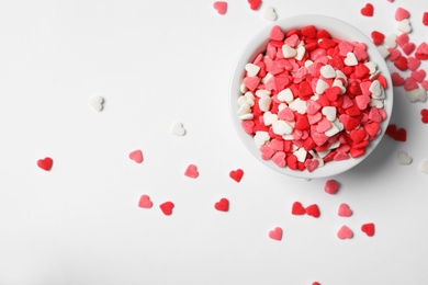 Bright heart shaped sprinkles and bowl on white background, flat lay. Space for text