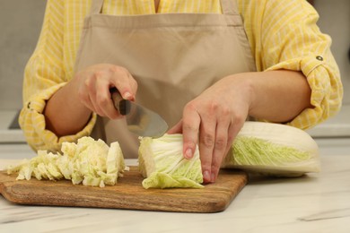 Photo of Woman cutting fresh chinese cabbage at table in kitchen, closeup