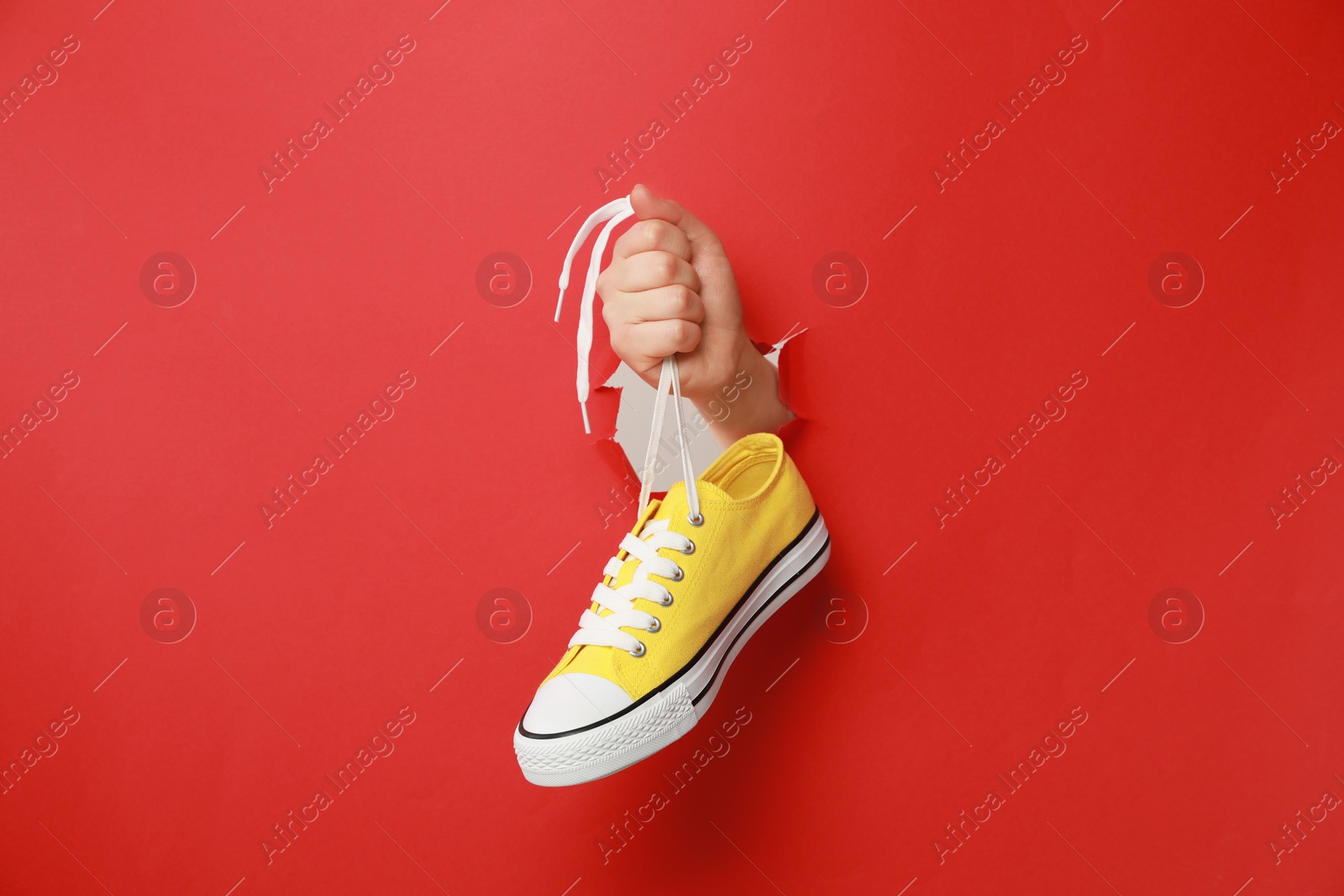 Photo of Woman holding yellow classic old school sneaker through hole in red paper, closeup