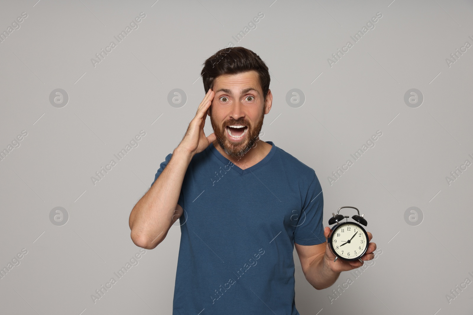 Photo of Emotional bearded man with alarm clock on light grey background. Being late concept