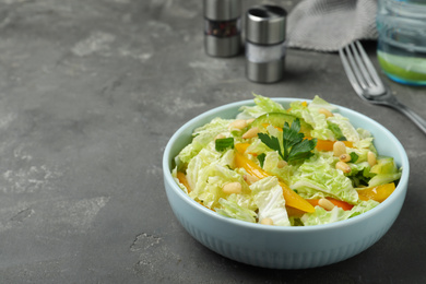 Bowl of fresh cabbage salad with bell pepper on grey table. Space for text