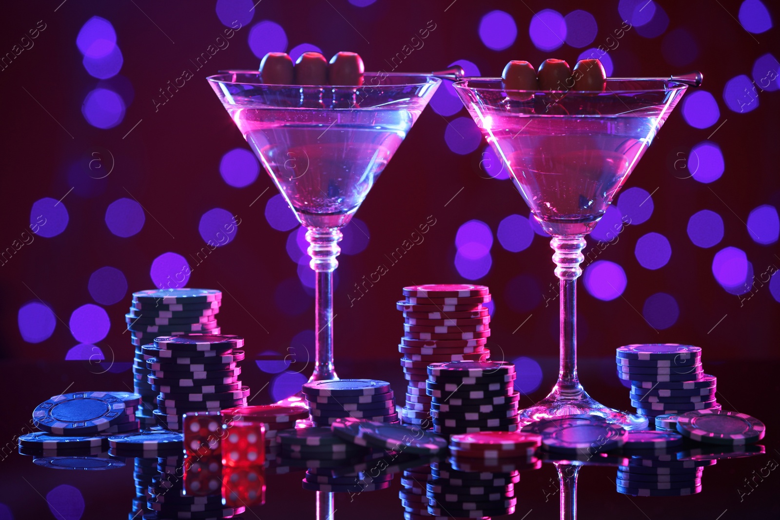 Photo of Cocktail, dice and casino chips on table against blurred lights