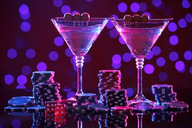 Photo of Cocktail, dice and casino chips on table against blurred lights