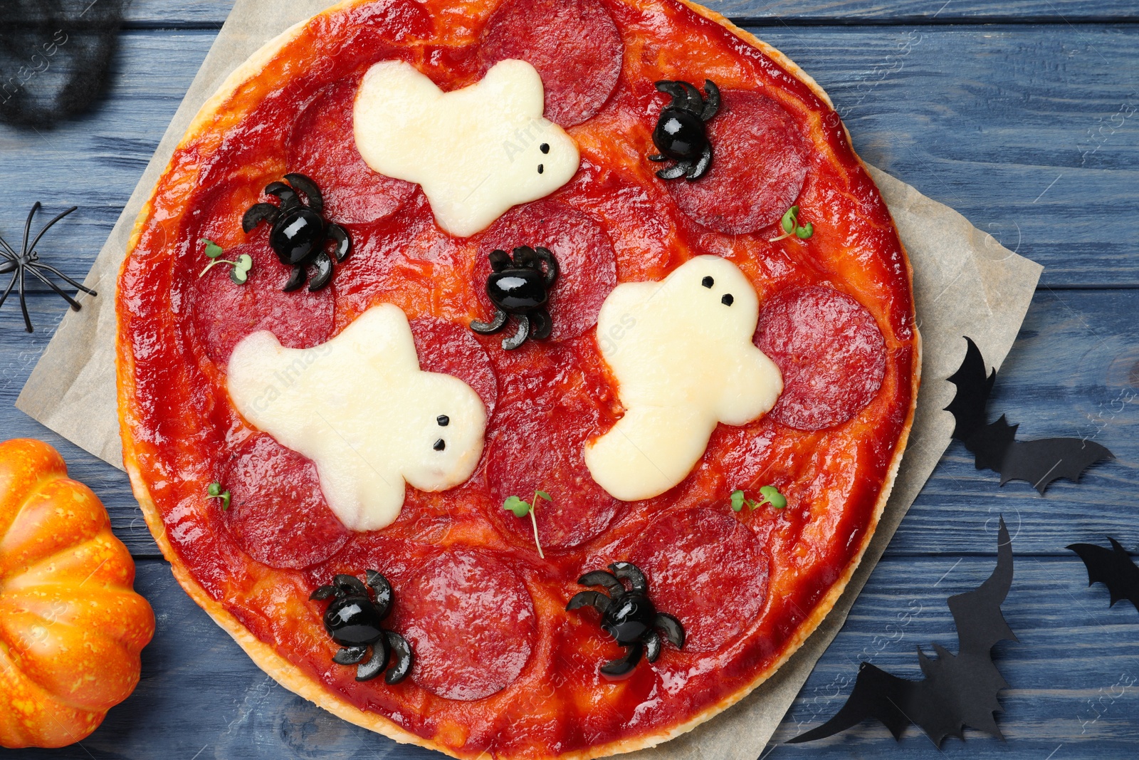 Photo of Cute Halloween pizza with ghosts and spiders served on blue wooden table, flat lay