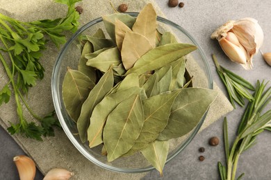Photo of Aromatic bay leaves in glass bowl, different herbs and spices on light gray table, flat lay