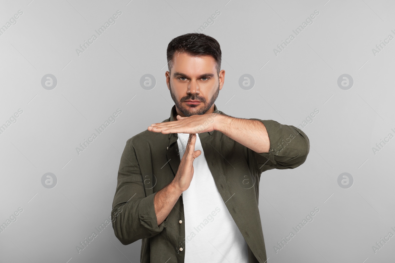 Photo of Handsome man showing time out gesture on light grey background. Stop signal