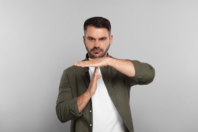 Photo of Handsome man showing time out gesture on light grey background. Stop signal