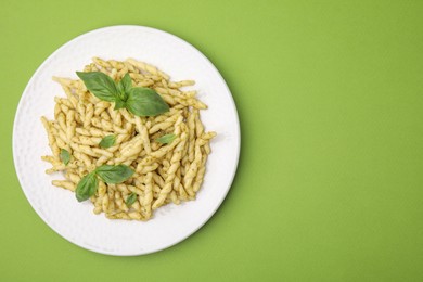 Plate of delicious trofie pasta with pesto sauce and basil leaves on light green table, top view. Space for text