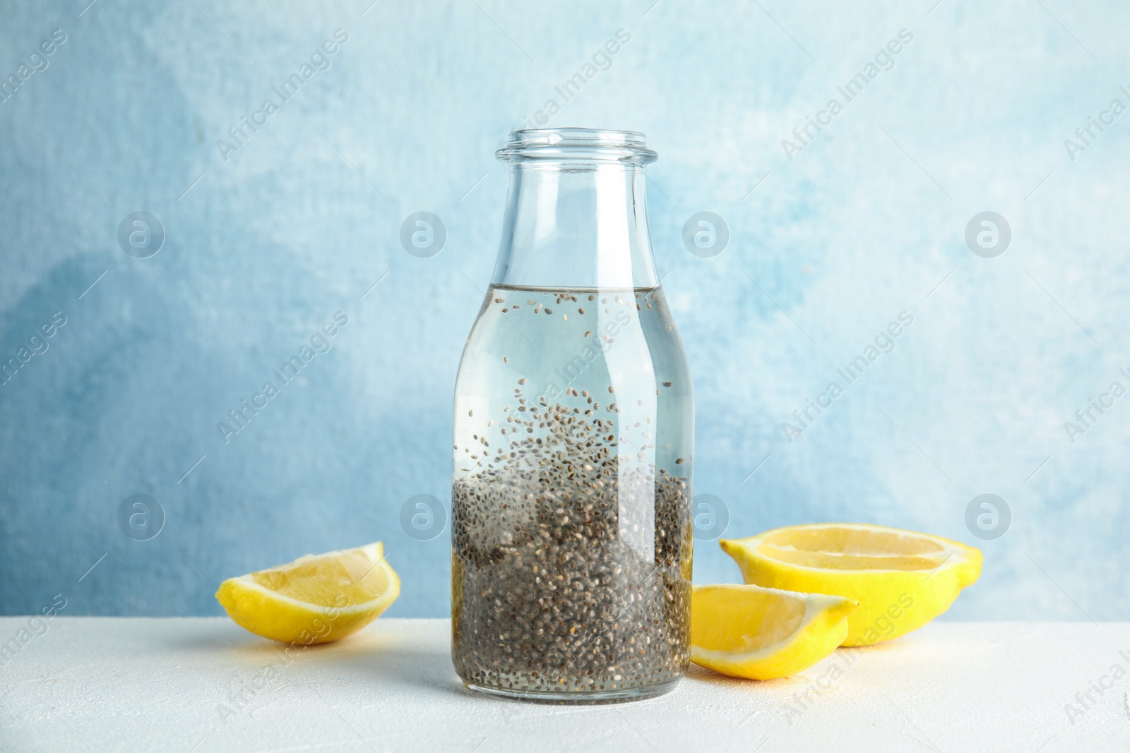 Photo of Bottle of water with chia seeds and lemon on table against color background