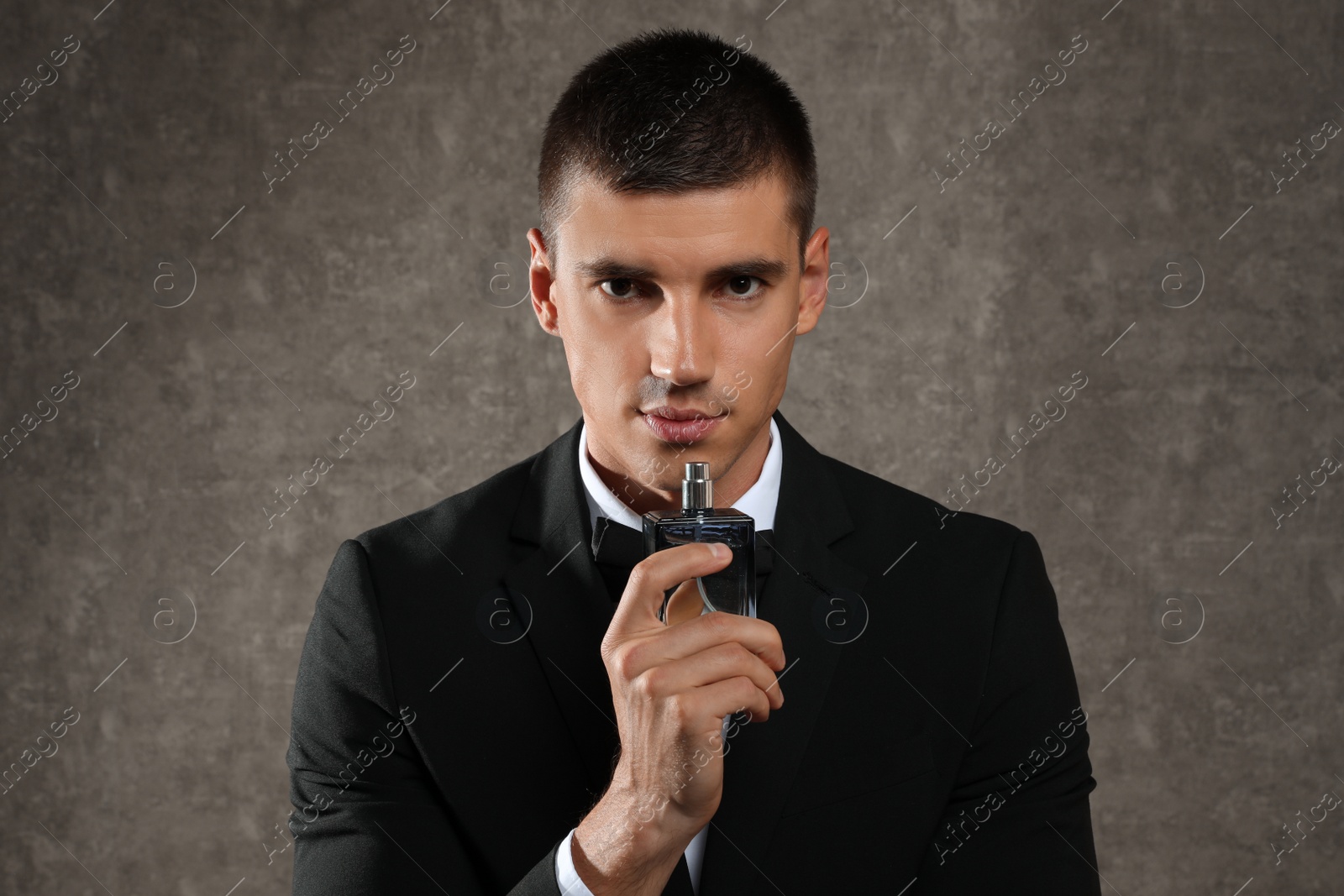 Photo of Handsome young man with bottle of perfume on grey stone background