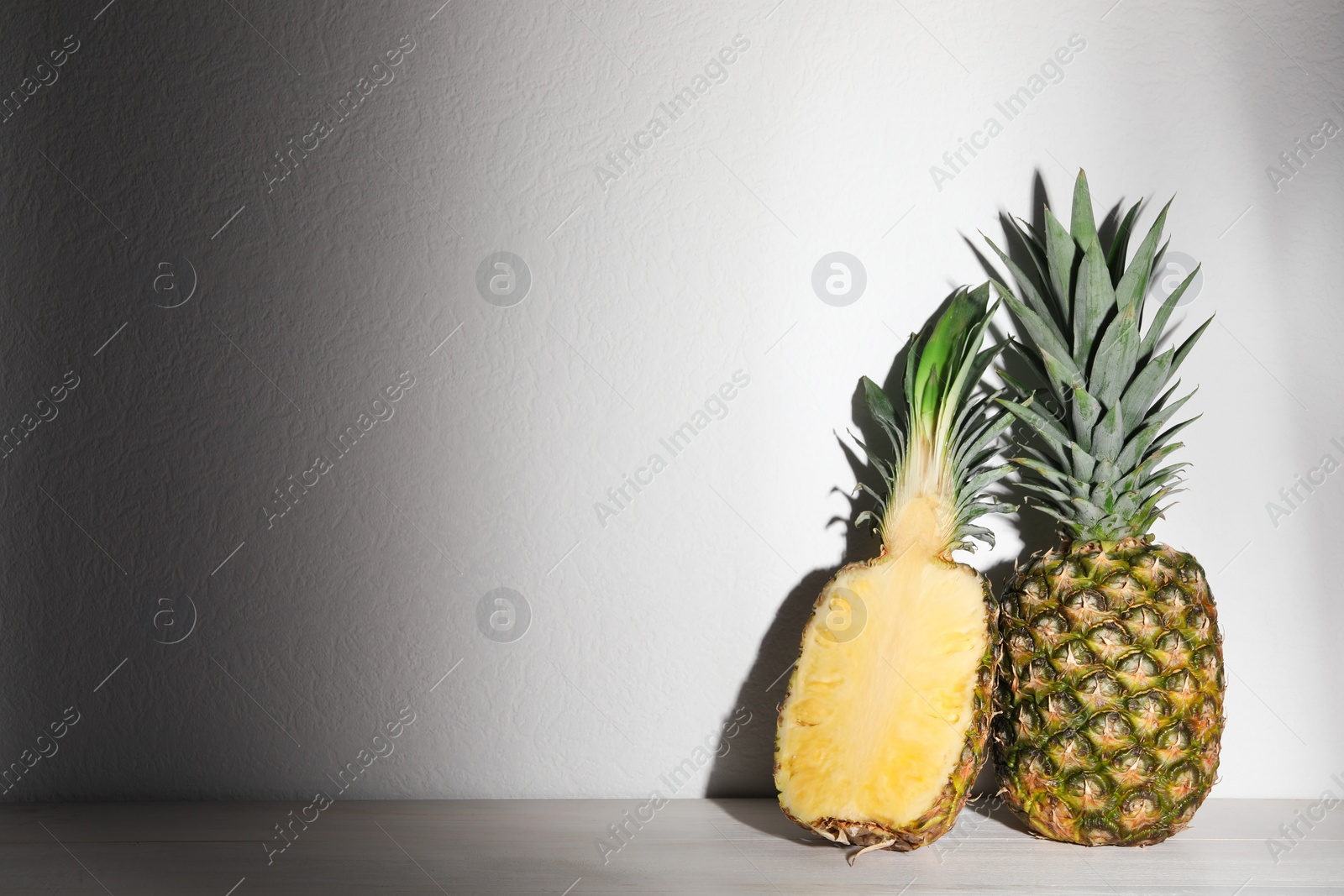 Photo of Whole and cut ripe pineapples on white wooden table. Space for text
