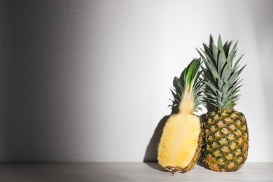 Whole and cut ripe pineapples on white wooden table. Space for text