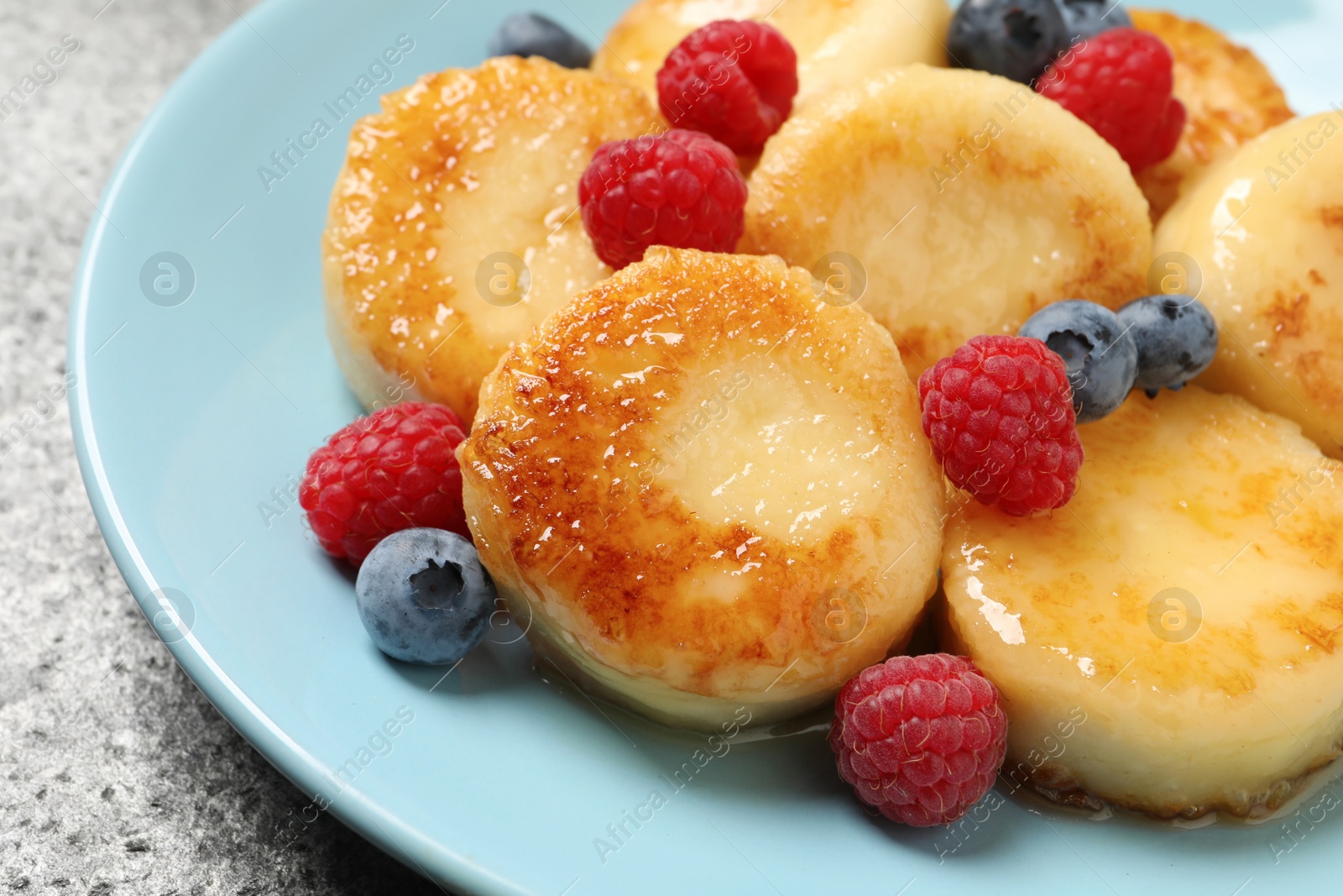 Photo of Delicious cottage cheese pancakes with fresh berries and honey on grey table, closeup