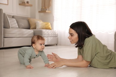 Photo of Happy young mother watching her cute baby crawl on floor at home
