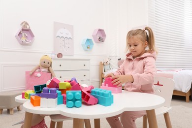 Photo of Cute little girl playing with colorful building blocks at table in room, space for text