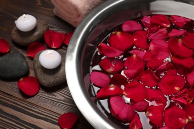 Bowl with water, red rose petals, stones and burning candles on wooden floor, closeup. Pedicure procedure