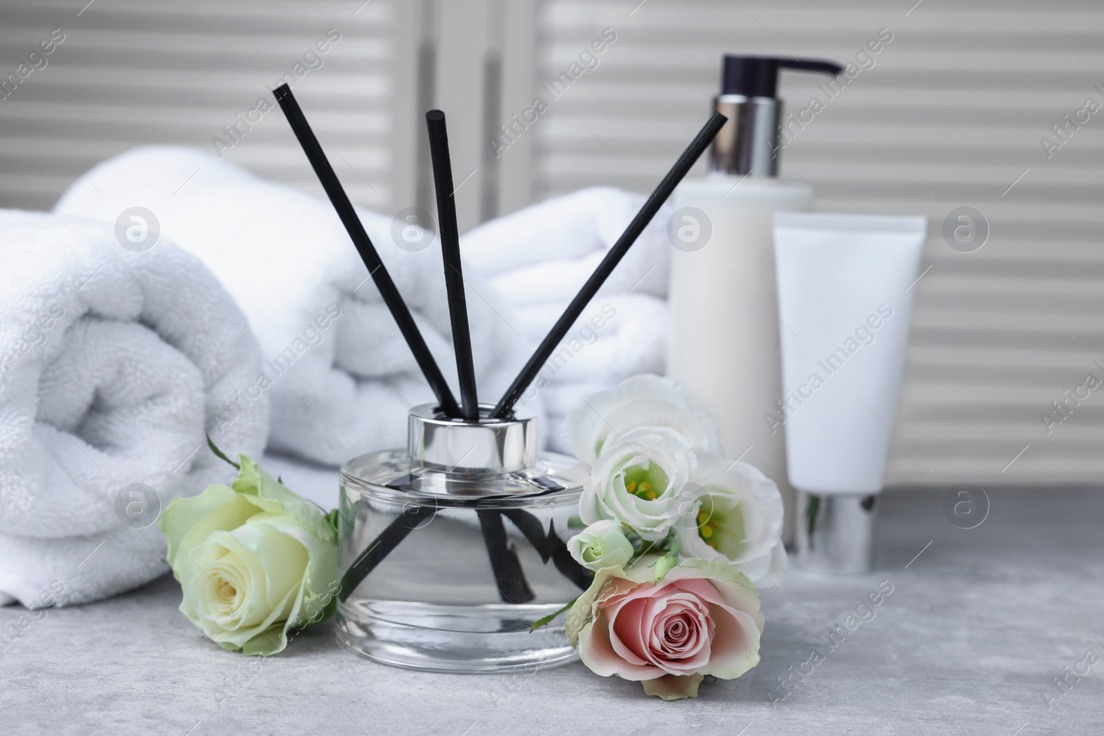 Photo of Towels, reed air freshener, cosmetic products and flowers on grey table indoors