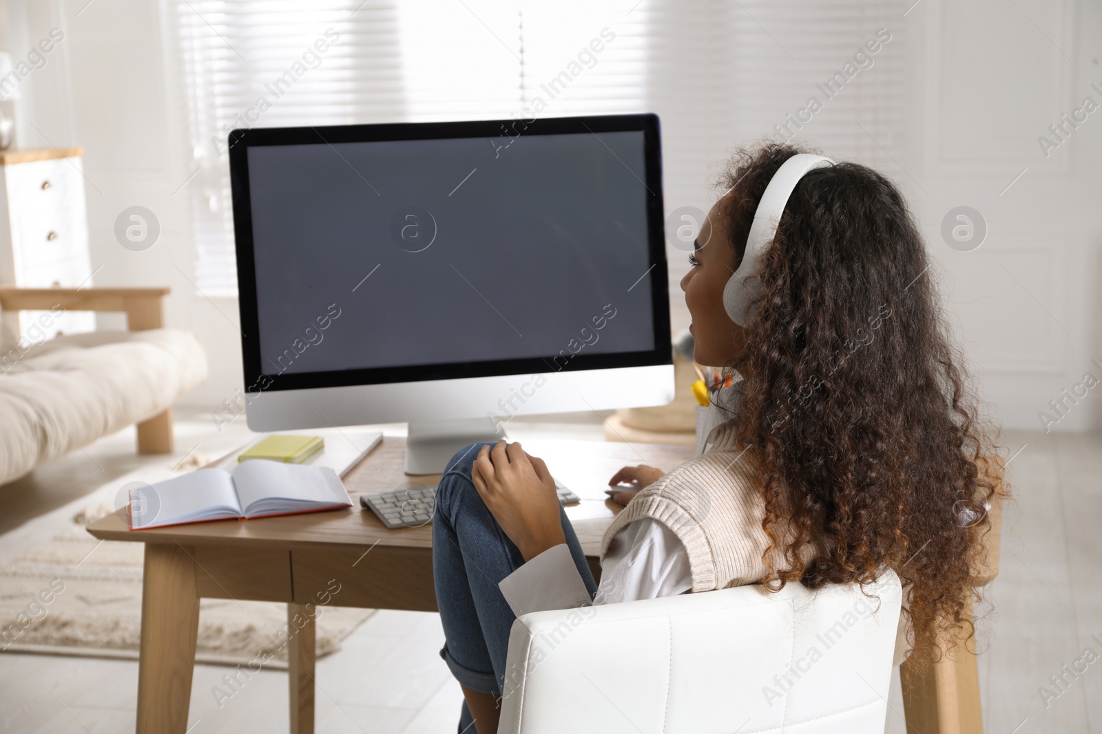 Photo of African American woman with headphones using modern computer for studying at home. Distance learning