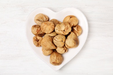 Plate with dried figs on white wooden table, top view. Healthy fruit