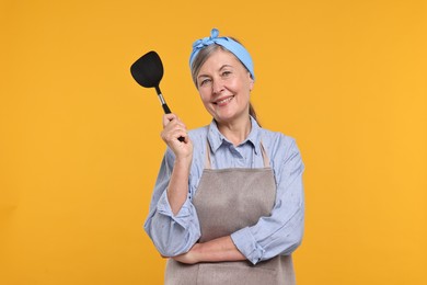 Photo of Happy housewife with turner on orange background