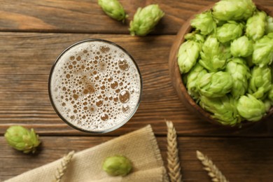 Glass of beer, fresh green hops and spikes on wooden table, flat lay